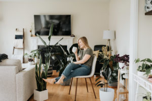 Woman relaxing with warm beverage in room full of house plants Woman relaxing with warm beverage in room full of house plants